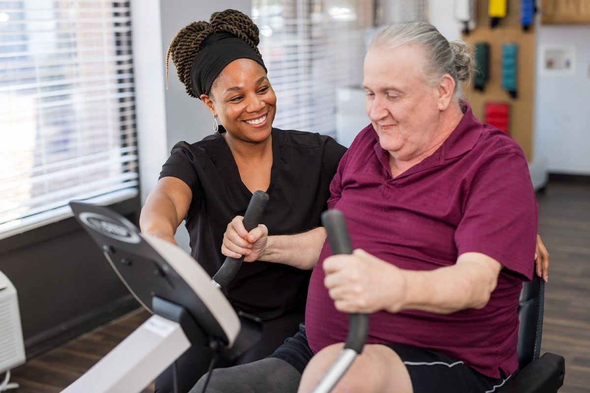PACS-300x200-woundcare Physical therapist working with patient on bike at Cedar Creek Post Acute