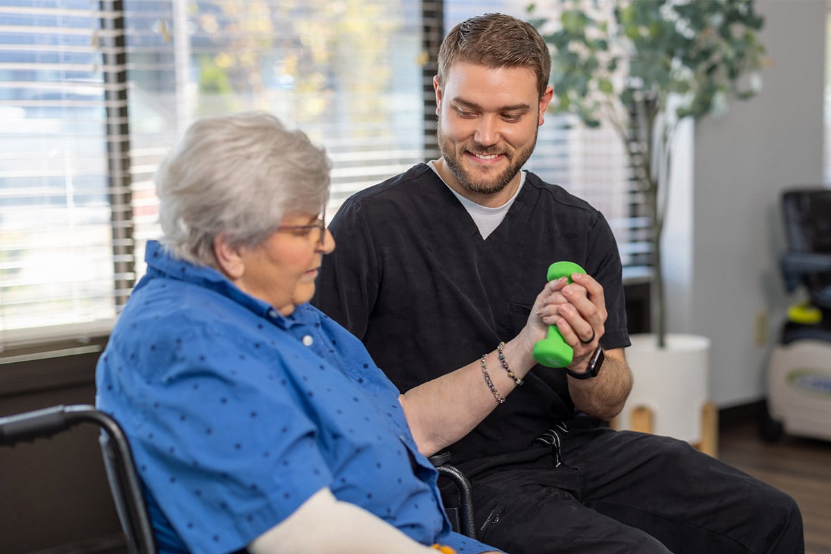 PACS-300x200-rehab2 Physical therapist helping patient hold dumbbell at Cedar Creek Post Acute